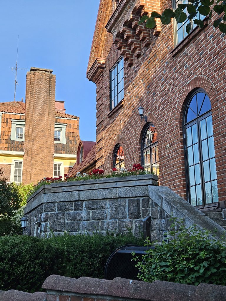 Punatiilinen jugend-tyylinen rakennus kaari-ikkunoilla Armfeltintiellä Eiran kaupunginosassa Helsingissä. Kuvassa myös puutarha-alue ja katunäkymää — kuvattu vuonna 2025.